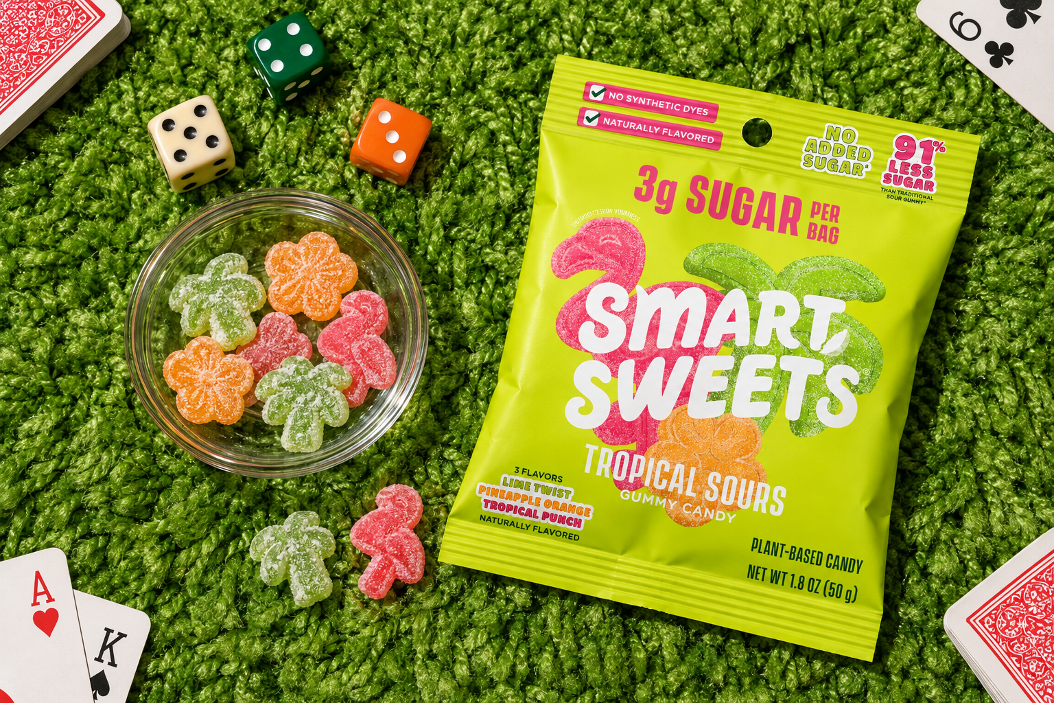 SmartSweets Tropical Sours with gummies, dice, and playing cards on a green rug